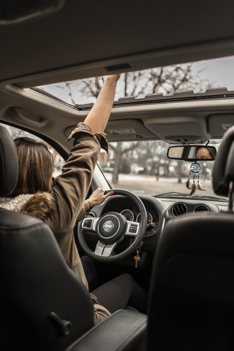 young driver raising her right hand inside black and brown auto